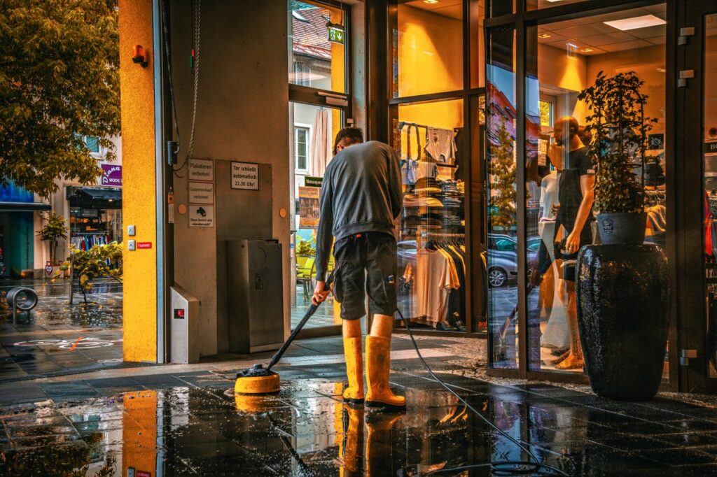 A man cleans the entrance of a store during a rainy day, reflecting urban life.